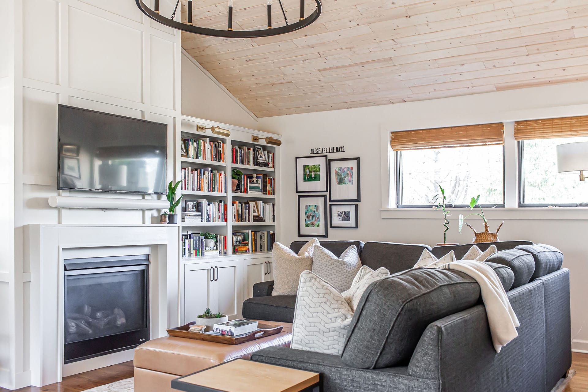 A cozy family room featuring a modern white fireplace with a mounted TV, built-in bookshelves, and a comfortable gray sectional sofa accented with plush pillows.