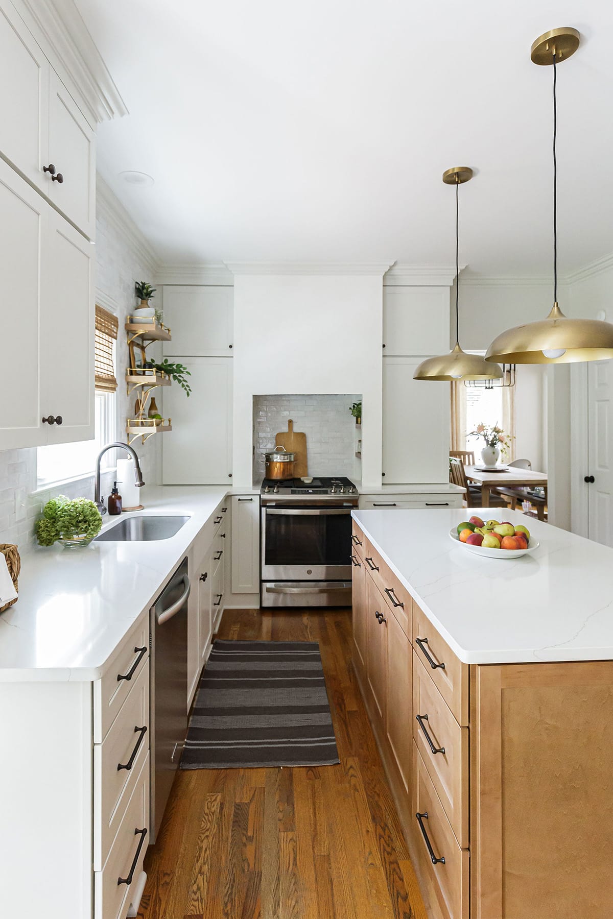 A sleek kitchen featuring a plaster hood over a stainless steel stove, warm wood island, and brass pendant lighting.