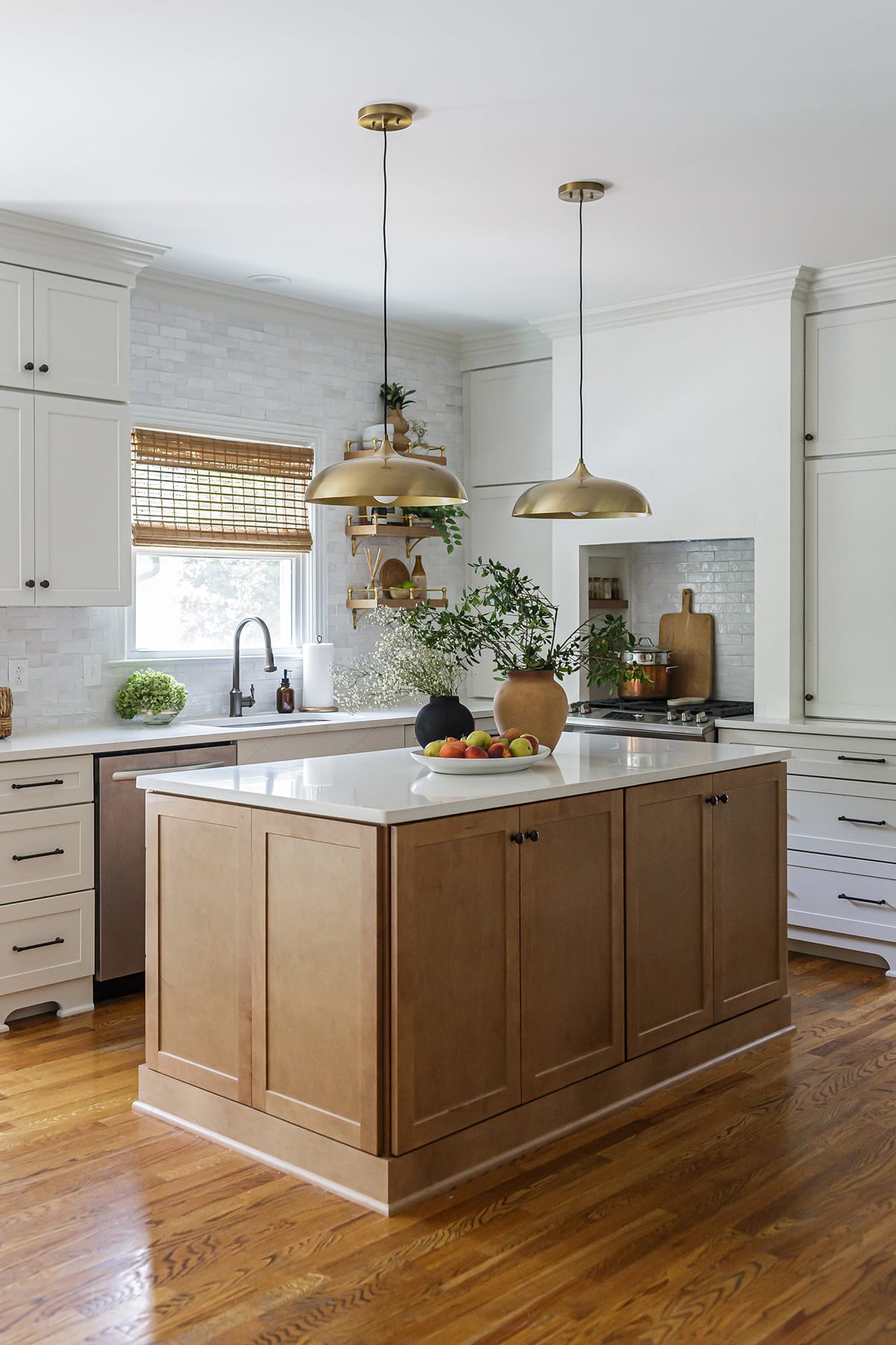 A modern kitchen featuring a natural wood island with a quartz countertop, brass pendant lights, and open shelving with brass accents above the sink.