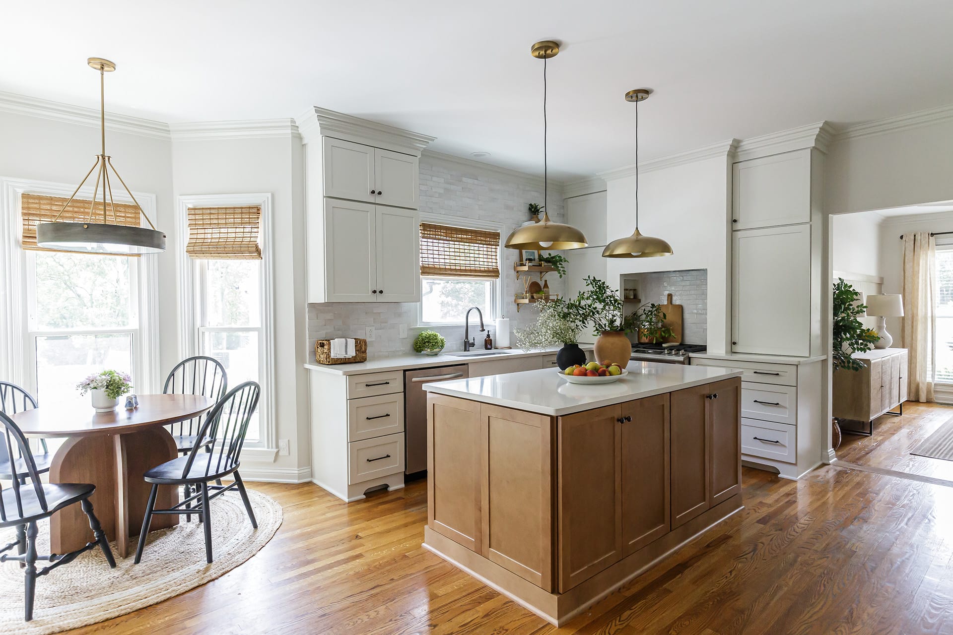 Sleek, open-concept kitchen with a modern edge featuring a natural wood island, brass pendant lighting, and a cozy breakfast nook featuring a round table and black spindle chairs.