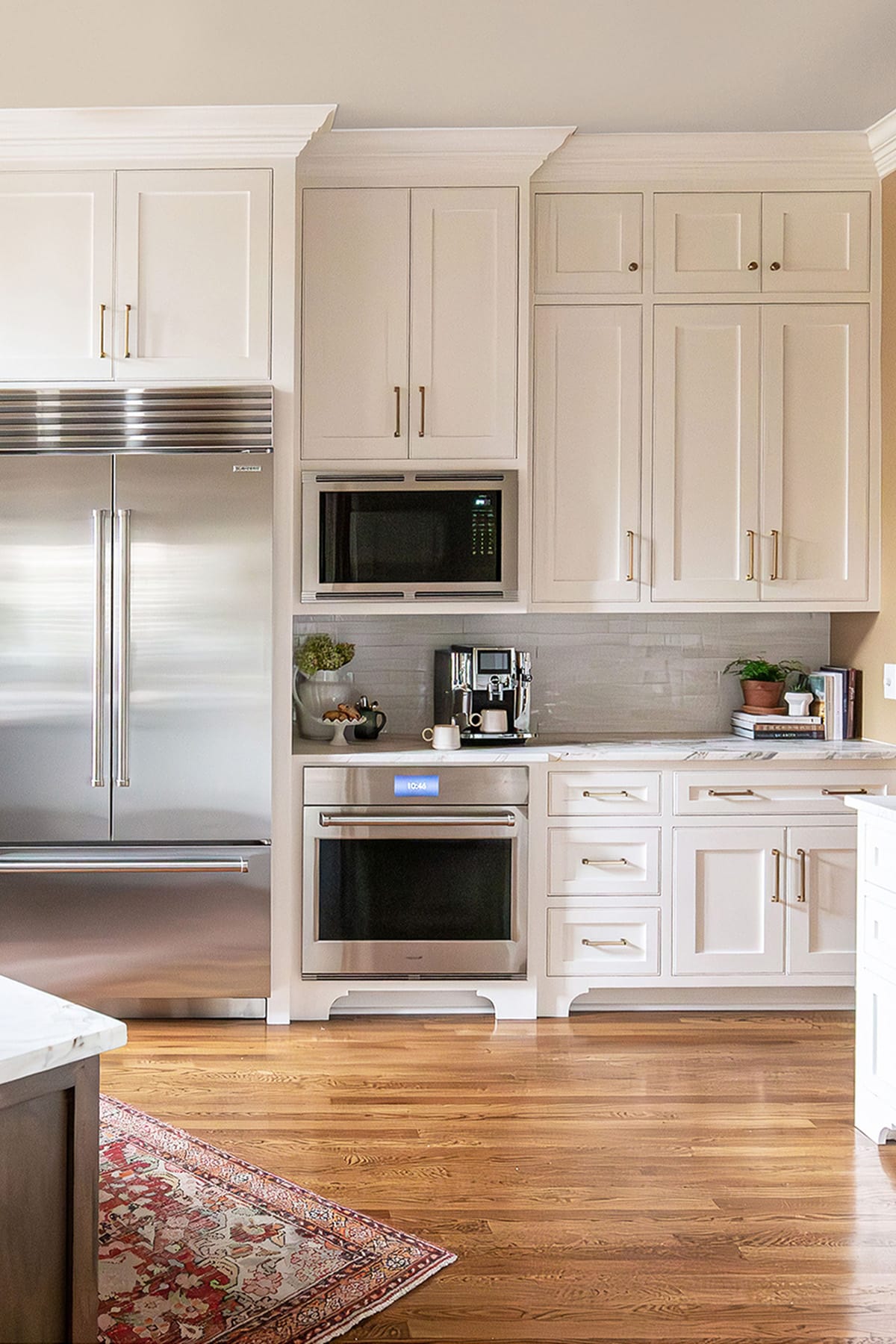 A kitchen wall featuring white cabinetry, stainless steel appliances, including a built-in oven, microwave, and refrigerator, with a marble countertop and coffee station.