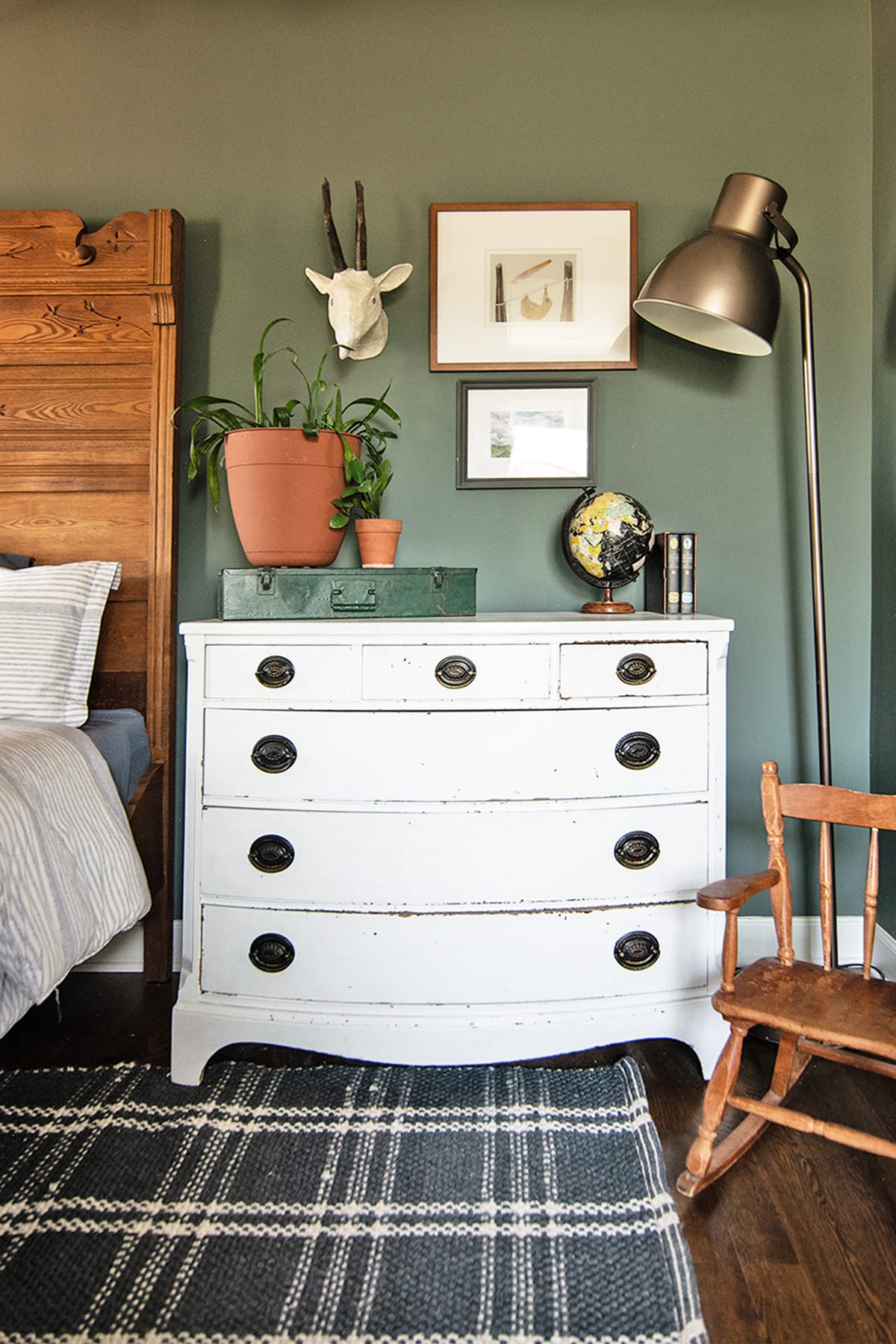 Vintage white dresser with globe, potted plants, and wall decor in a child's bedroom.