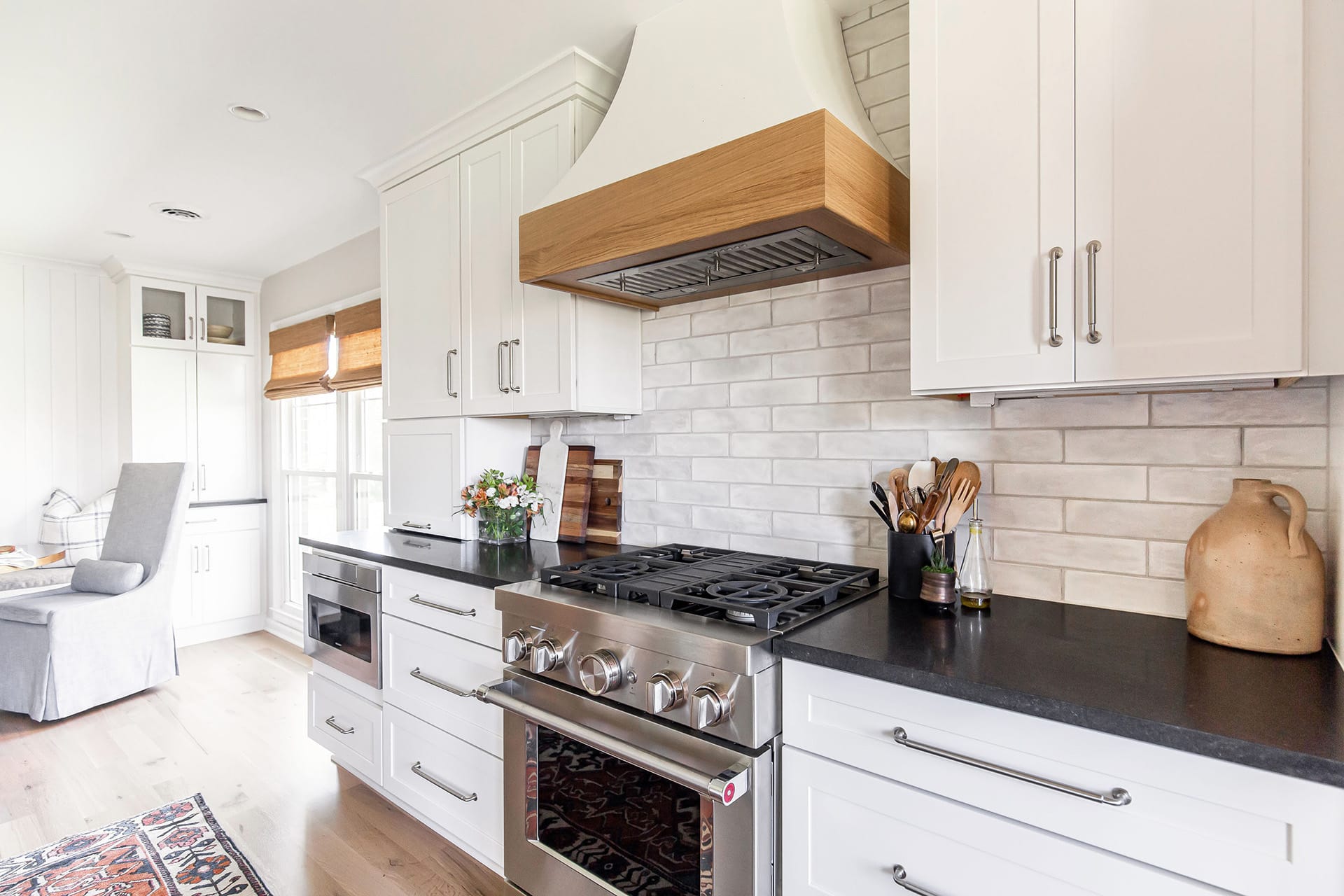 Elegant farmhouse kitchen with a custom wooden range hood, white cabinetry, and a sleek black countertop, styled with fresh flowers and rustic accents.