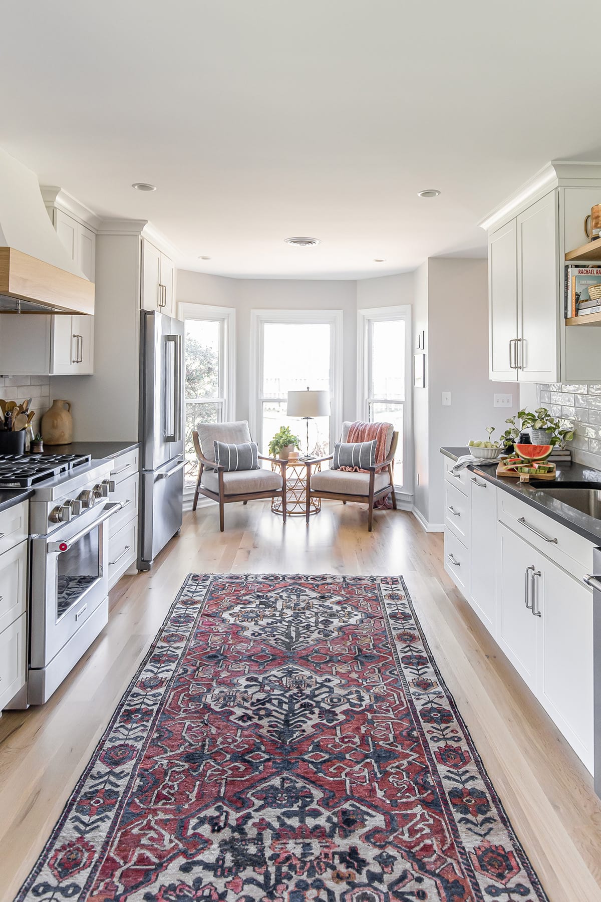 Bright farmhouse kitchen with an oriental rug, bay window seating, and modern white cabinetry.