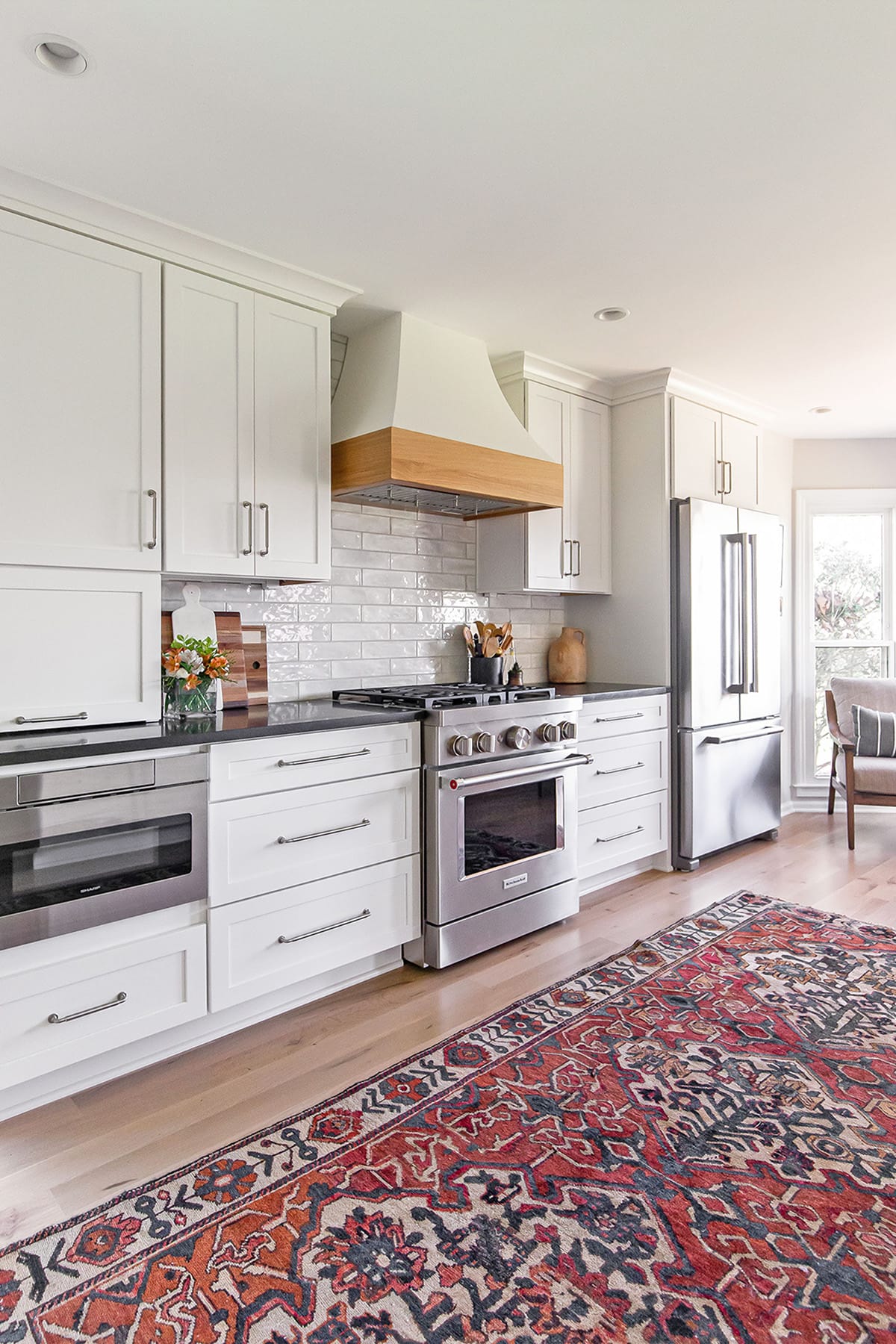 Farmhouse kitchen range wall with white cabinetry, subway tile backsplash, and a wooden range hood.