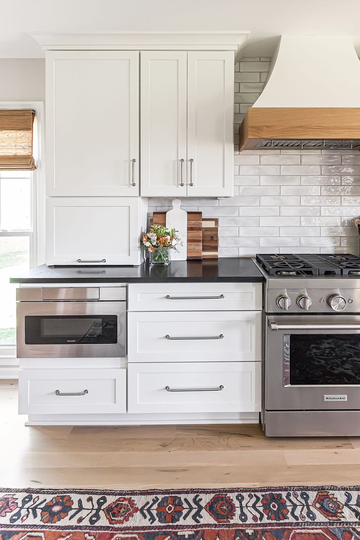 Farmhouse kitchen range and microwave with white cabinetry, dark countertops, and a subway tile backsplash.