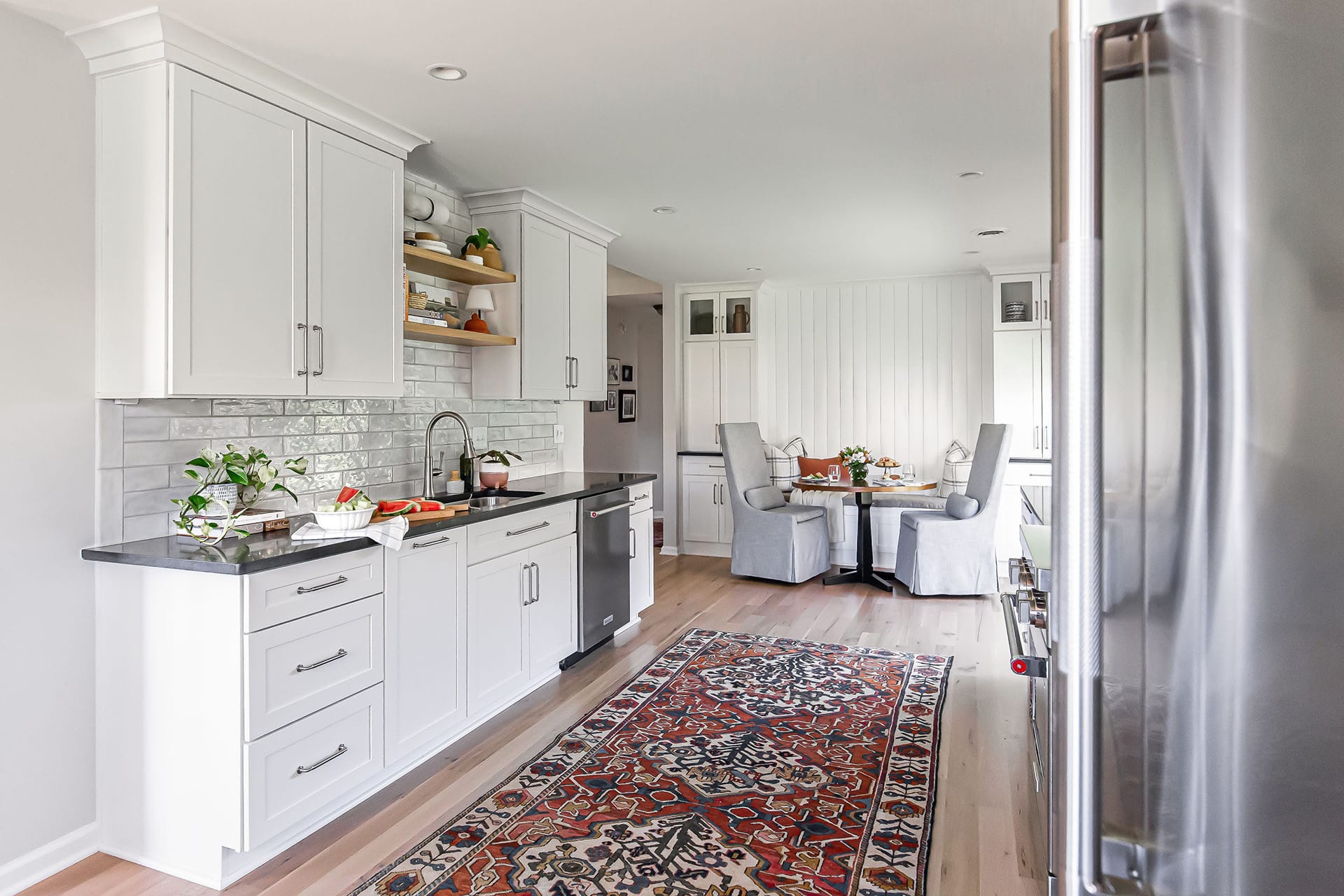 Farmhouse kitchen sink wall with white cabinetry, open shelves, subway tile backsplash, and a cozy breakfast nook.