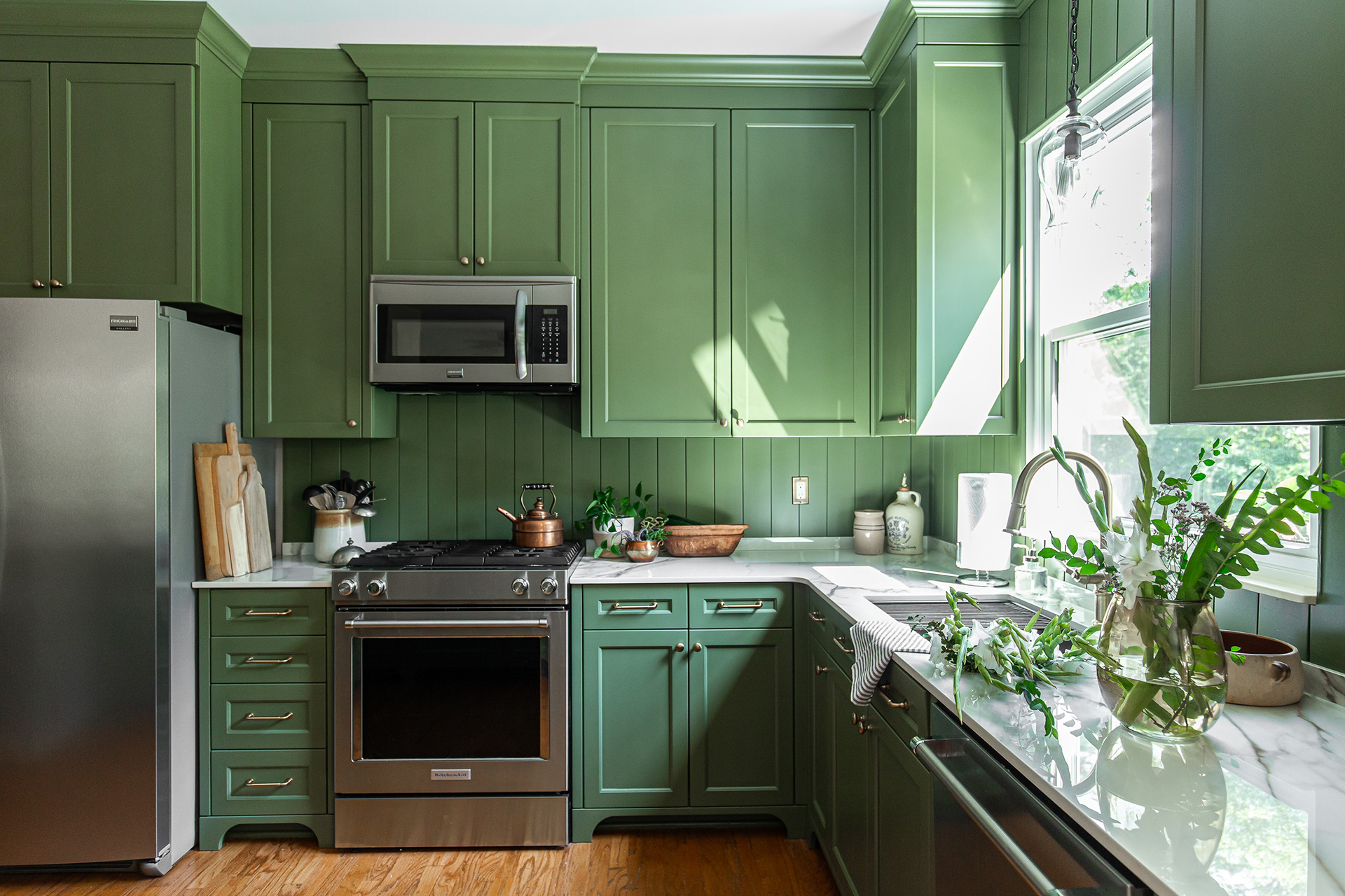 Stylish kitchen with green cabinetry, porcelain countertops, stainless steel appliances, and natural light enhancing fresh greenery.