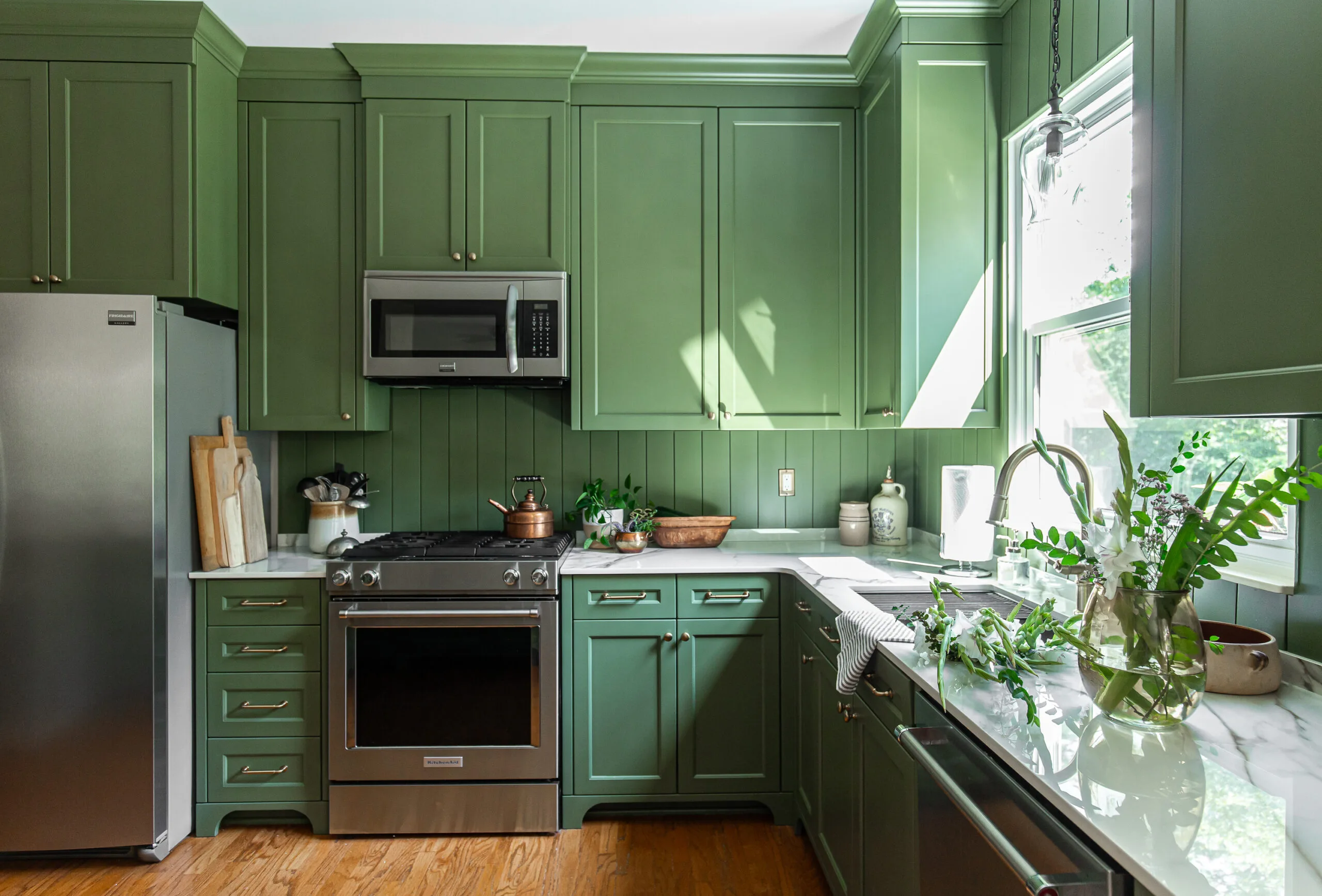 Stylish kitchen with green cabinetry, porcelain countertops, stainless steel appliances, and natural light enhancing fresh greenery.