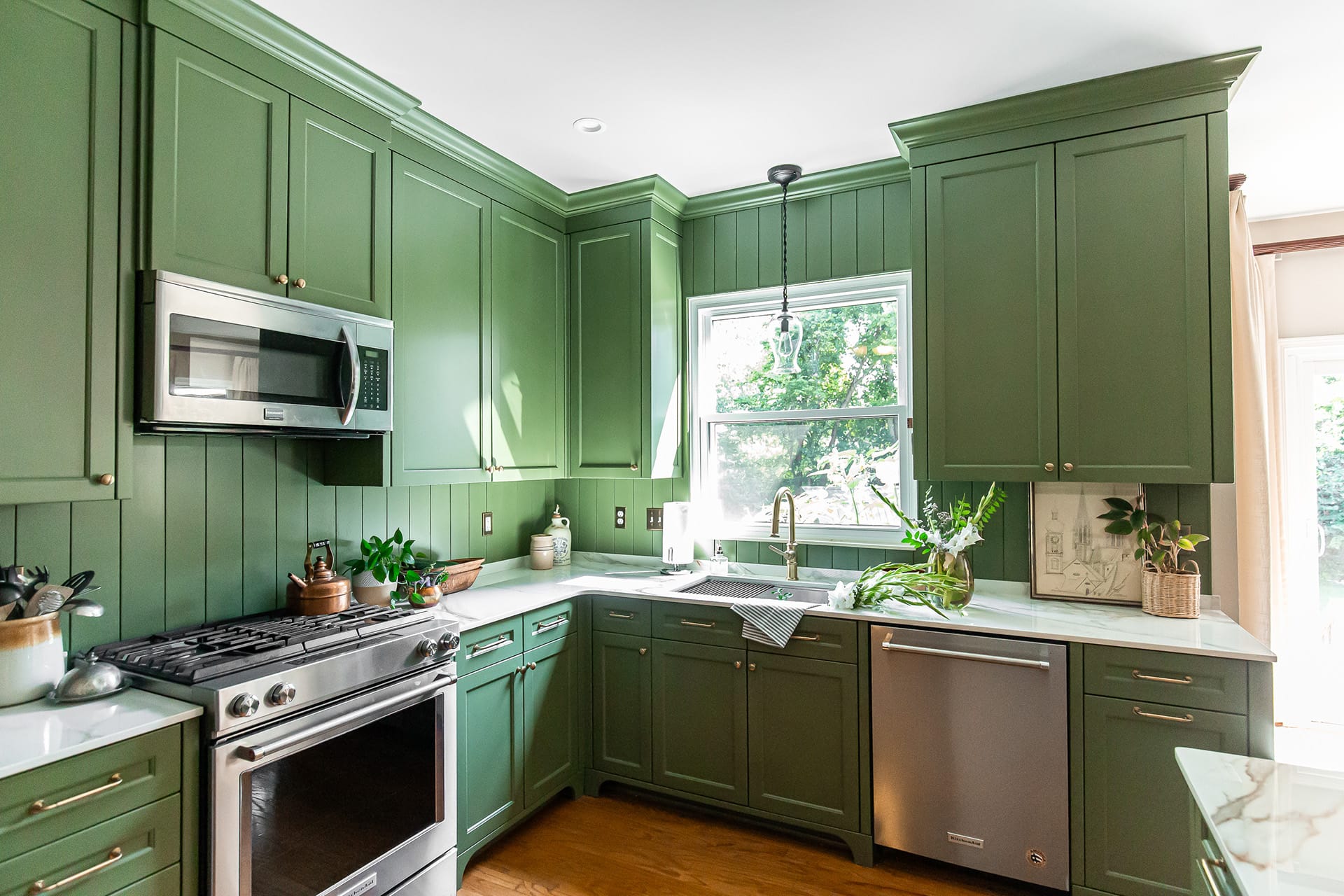 Kitchen with green cabinetry, stainless steel appliances, porcelain countertops, and a large window bringing in natural light.