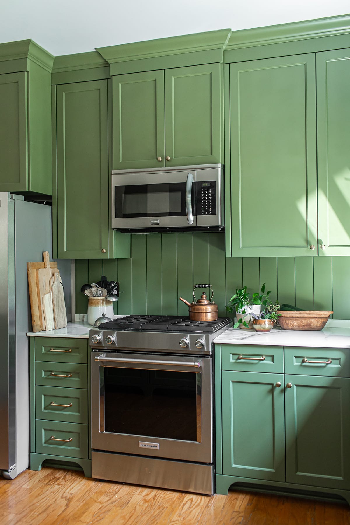 Green kitchen with stainless steel range and microwave, porcelain countertops, and natural wood and greenery accents.