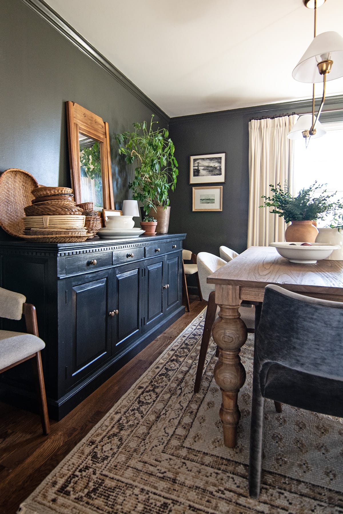 A sophisticated dining room with a black buffet adorned with woven baskets and pottery, a wooden dining table with turned legs, and green walls creating a cozy, inviting atmosphere.