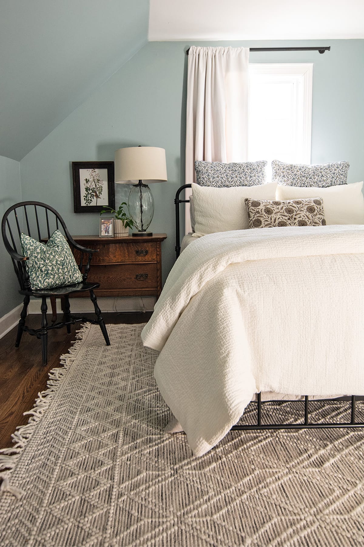 Cozy guest bedroom with a metal bedframe, vintage wood nightstand, and soft blue walls.