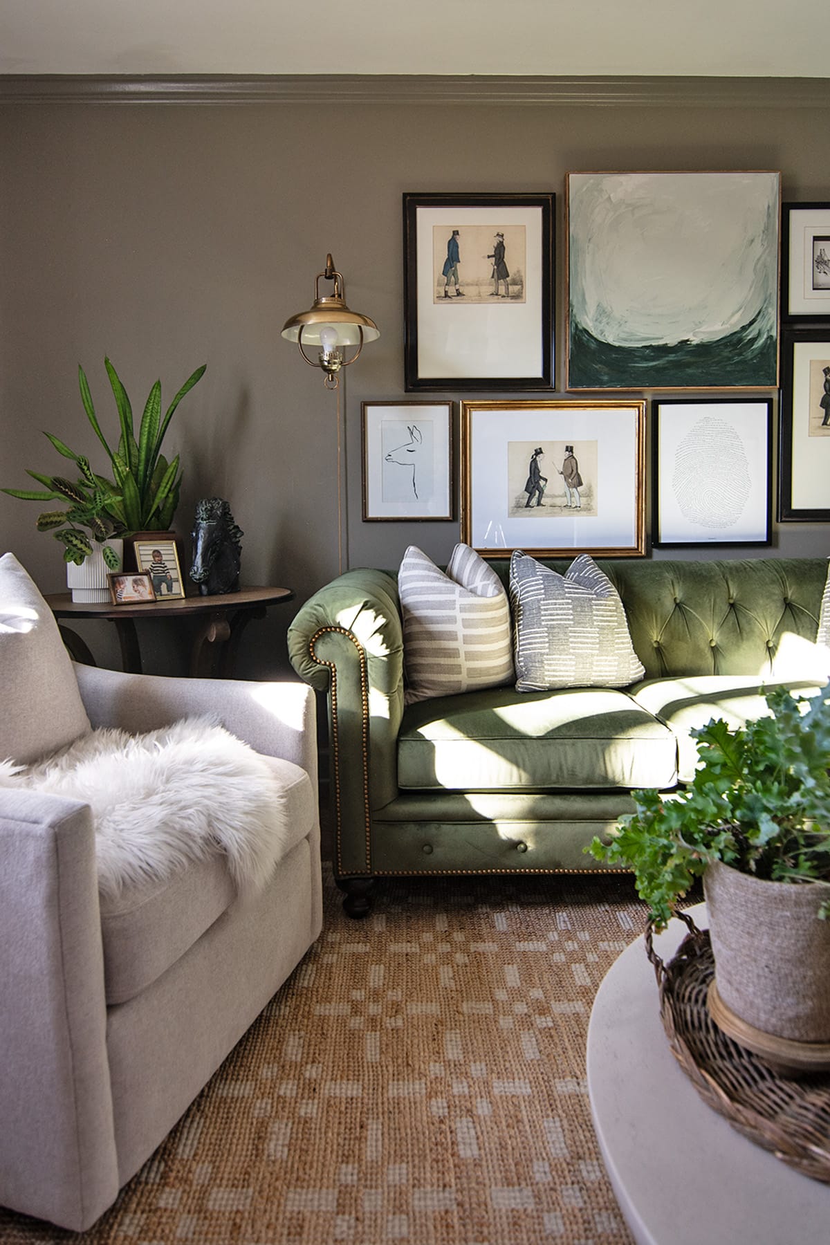 A close-up of a cozy living room corner featuring a green tufted Chesterfield sofa, a neutral armchair with a faux fur throw, and a gallery wall of curated art in various frames.