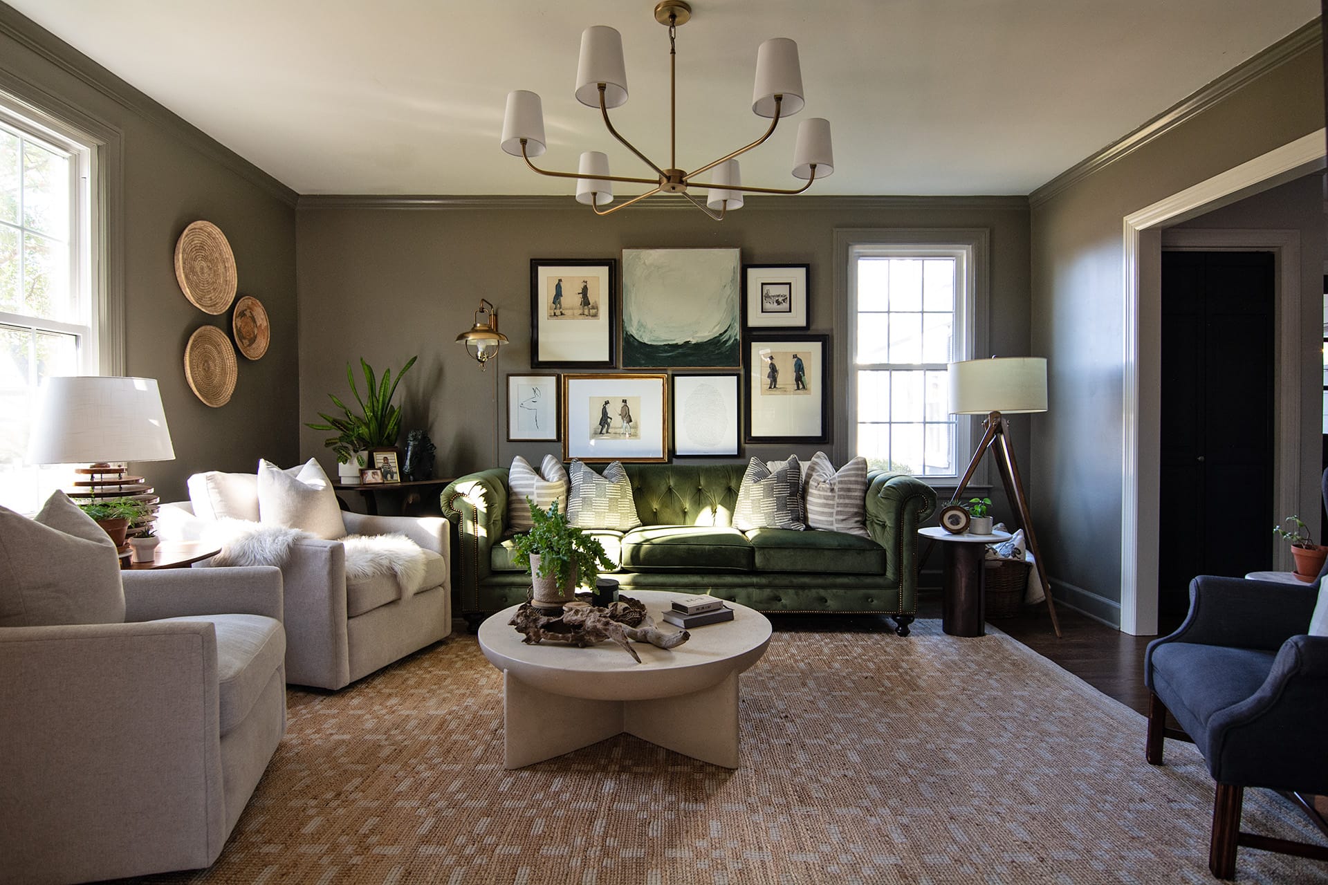 Classic charm reimagined in this Franklin colonial home with warm living room featuring a green tufted Chesterfield sofa, a gallery wall of eclectic artwork, neutral armchairs, and a round modern coffee table atop a textured rug.