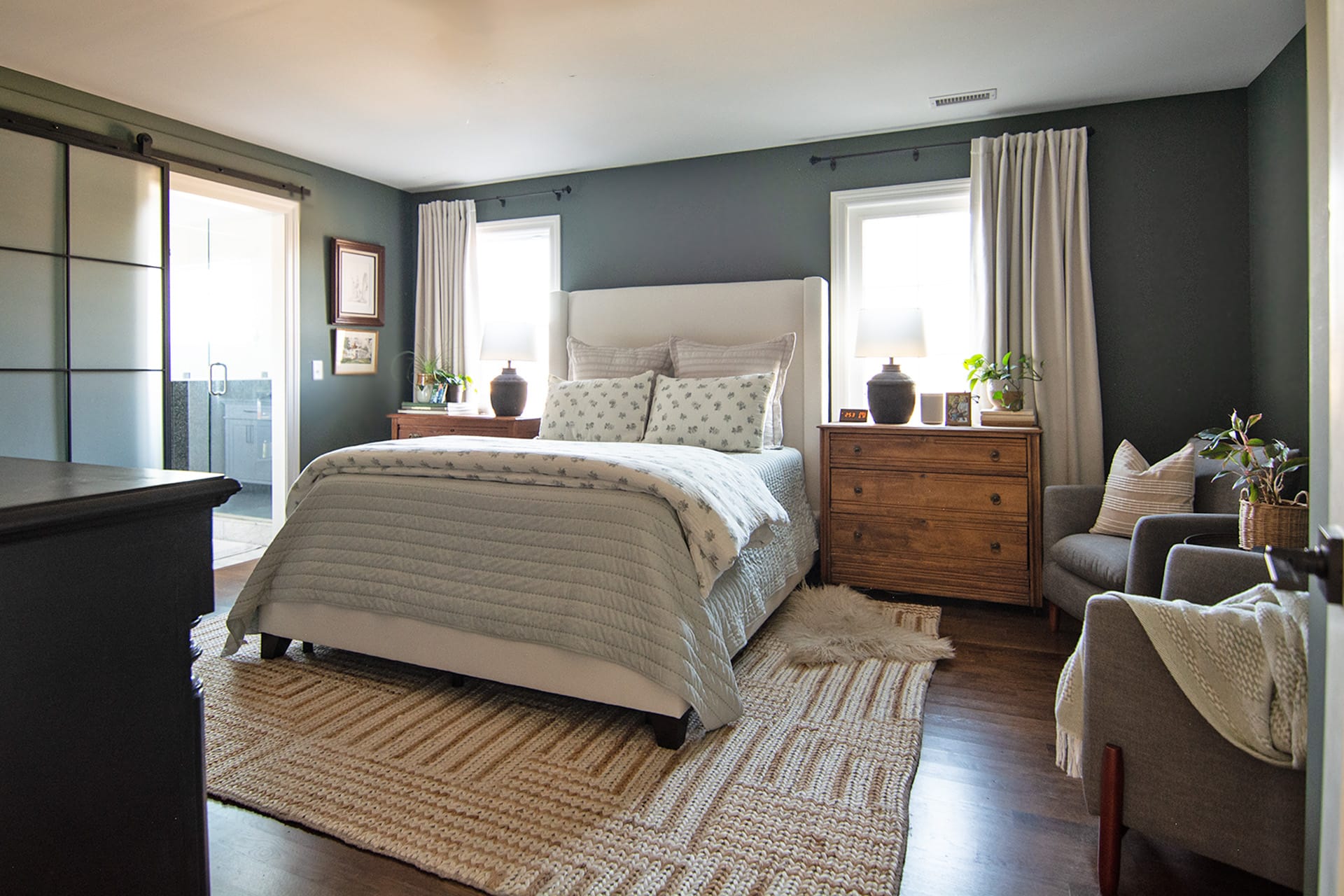 A serene primary bedroom with a neutral upholstered bed, layered bedding, wooden nightstands, and cozy accents such as a textured rug and armchair.