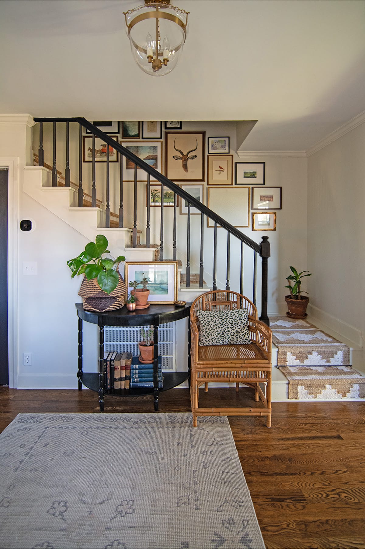 Gallery wall along a stairwell with a wicker chair, black console table, and plants.