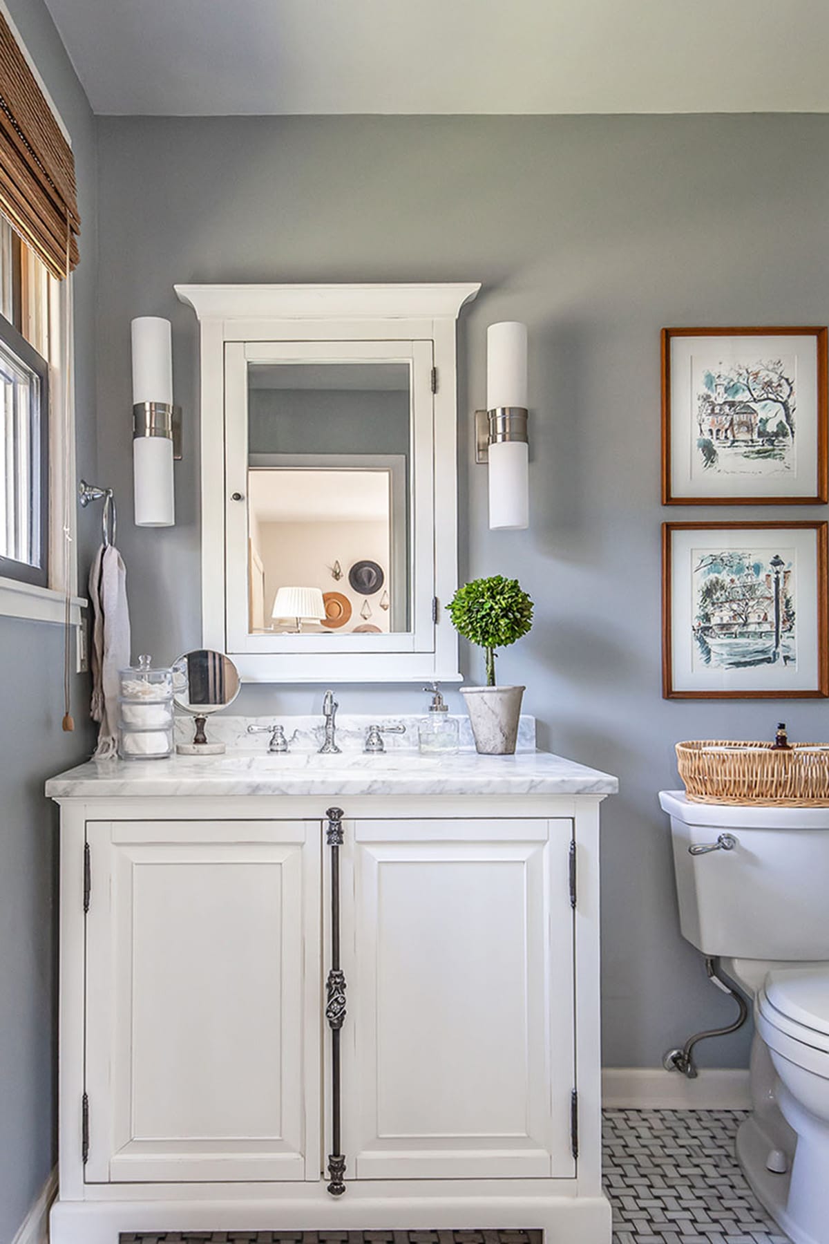 A bright and elegant bathroom featuring a white marble-topped vanity, a mirrored cabinet, and gray walls adorned with framed artwork.