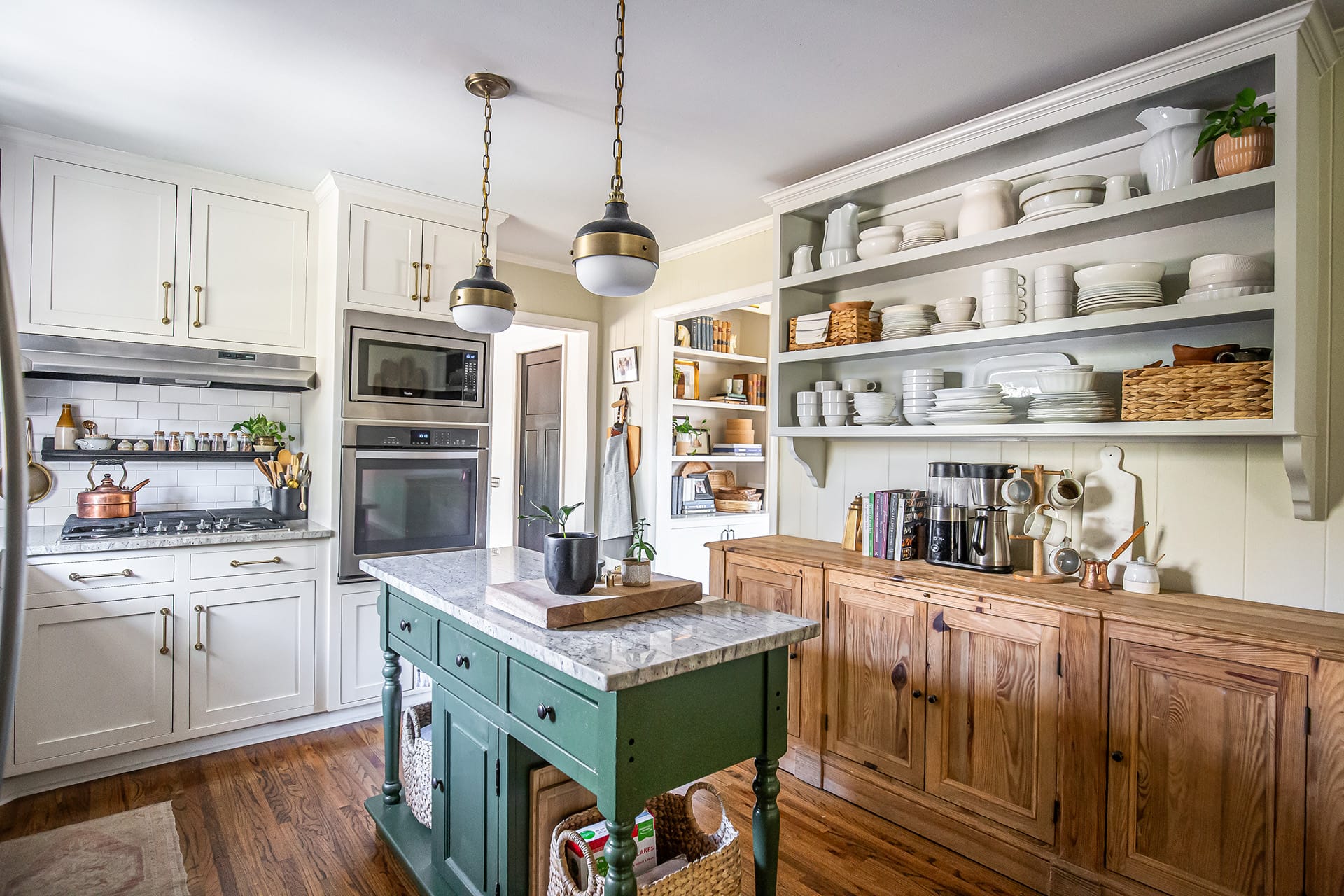 A beautifully designed kitchen featuring a green island with a marble countertop, open shelving filled with white dinnerware, and a cooking area with brass accents.