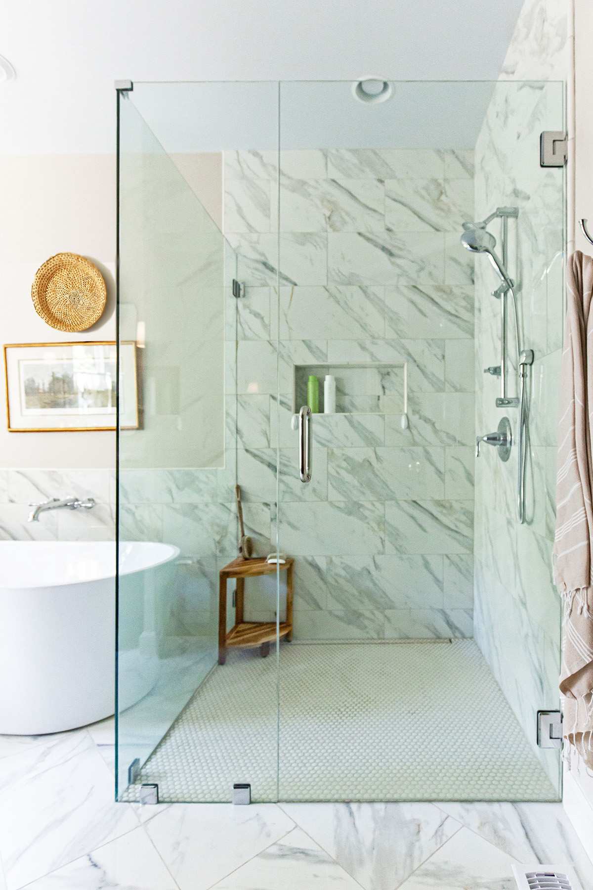 Primary bathroom with a glass-enclosed shower, porcelain tile, freestanding bathtub, and warm neutral decor.