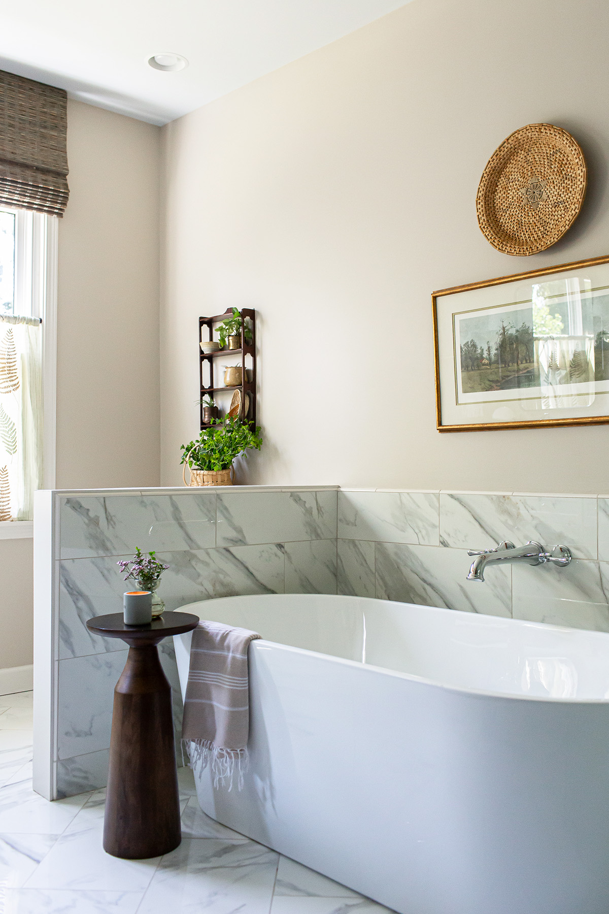 Freestanding bathtub with porcelain tile surround, wooden accent table, greenery, and woven wall decor in a serene bathroom.