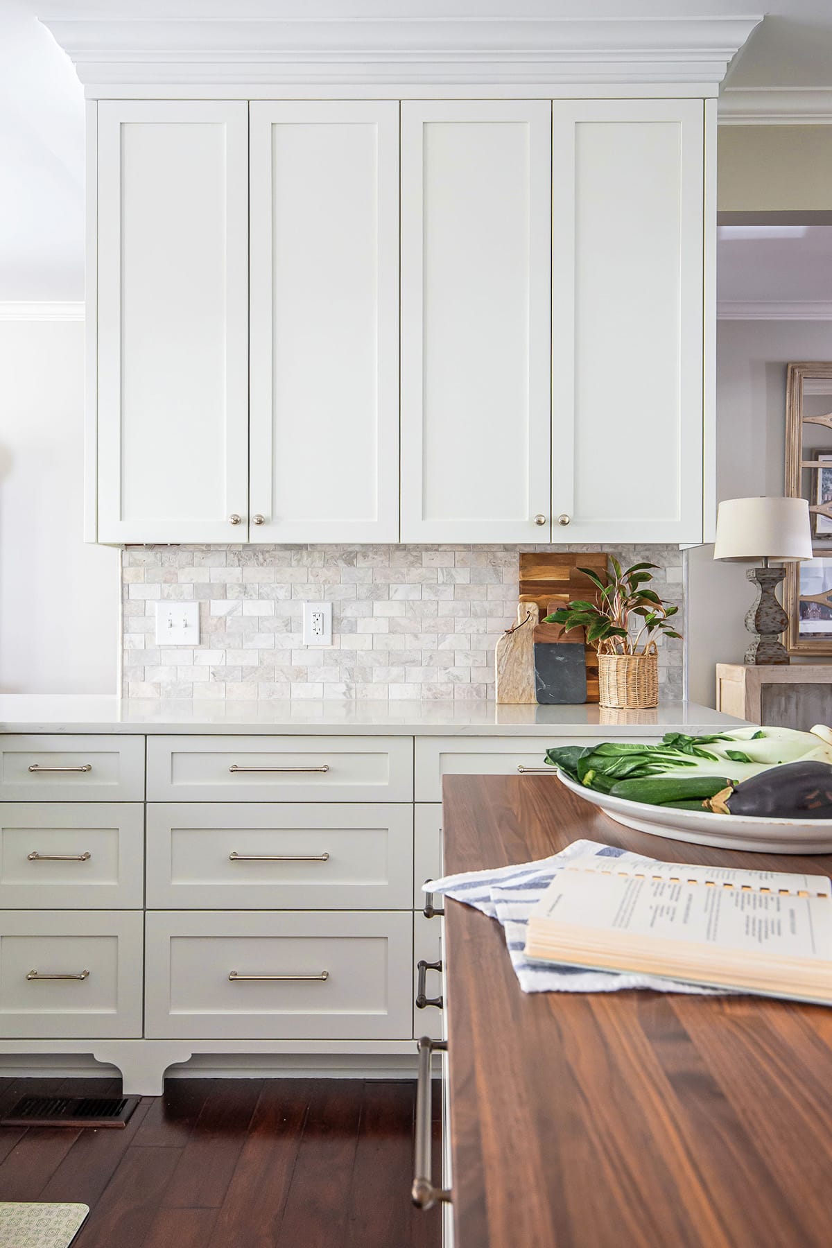 A kitchen with white cabinetry, a marble-style backsplash, and a warm wood countertop on the island, styled with fresh vegetables and natural accents.